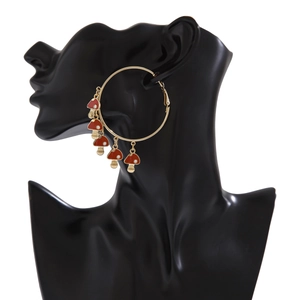 Close-up of gold oversized hoop earrings with red mushroom charms on model