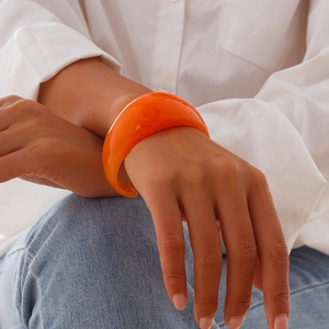 Close-up of a chunky semi-transparent bright orange acrylic bracelet on a model's wrist