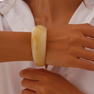 Detail showing irregular wide acetate bangle with amber texture on a woman's wrist