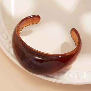 Macro shot of an amber tortoiseshell acrylic open bangle on a ceramic display