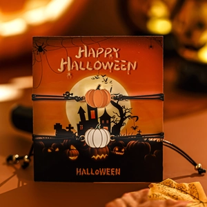 Dettaglio dei ciondoli a zucca di Halloween su bracciali intrecciati neri con carta