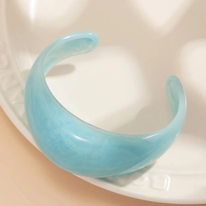 Macro view of light blue marble textured acrylic open cuff bracelet on ceramic tray