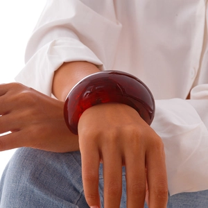 Close-up of wide deep red resin bangle with amber texture on a female wrist