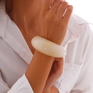 Close-up of wide cream acrylic cuff bracelet with marble texture on a model's wrist