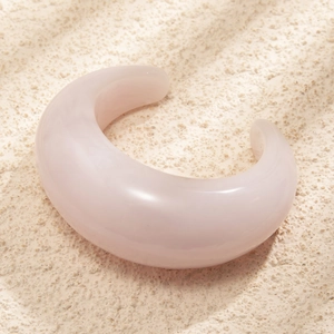 Macro detail of a wide semi-transparent pink acrylic C-shaped bangle in natural light