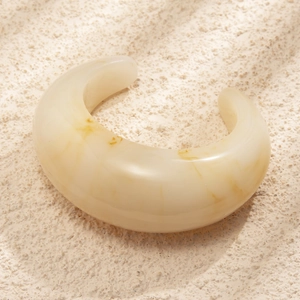 Chunky cream marble acetate resin open bangle with amber texture on a stone base