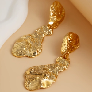 Nahaufnahme goldener geometrischer Tropfenohrringe mit gehämmerter Lavastruktur