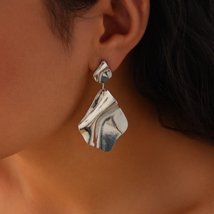 Détail de boucles d'oreilles en métal argenté martelé irrégulier sur l'oreille