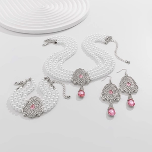 Detalle de conjunto de collar, pulsera y pendientes de perlas con gemas rosa en blanco