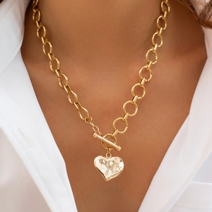 Detail van goudkleurige dikke ketting met hartvormige hanger en T-sluiting bij een model