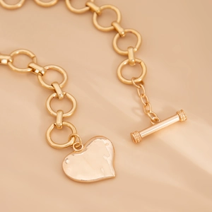 Detail van een goudkleurige schakelketting met hartjesbedel en OT-kapittel sluiting