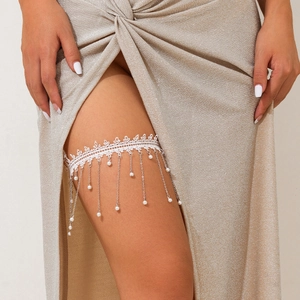 Detailansicht eines weißen Spitzen-Strumpfbands mit Metallkettenfransen und Perlen