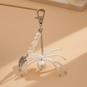 Macro detail of white pearl spider keychain with intricate hollow spider web charm