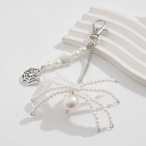 Detailed view of a pearl spider keychain with metallic web charm on a white stone background