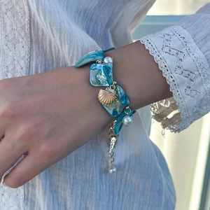 Dettaglio di un bracciale da spiaggia con elementi a conchiglia blu e perle