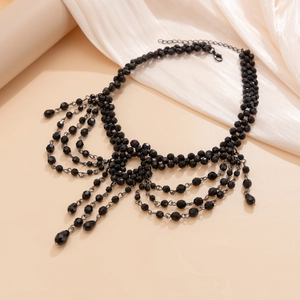 Detail of layered black beaded necklace with vintage cross tassel and lobster clasp closure
