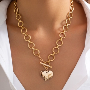 Detailopname van een gouden hartvormige punk ketting met OT-sluiting gedragen door model