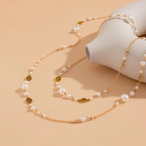 Detail of long pearl necklace with gold chain and circular charms on a white vase