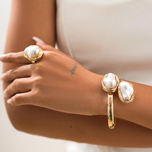 Gros plan sur un ensemble de bijoux en perles baroques avec bague dorée et bracelet ouvert