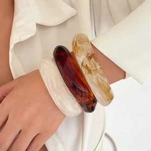 Close-up of chunky translucent resin bangles in amber and marble tones on wrist
