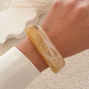 Close-up of translucent amber marble acrylic bangle worn on wrist over plush background