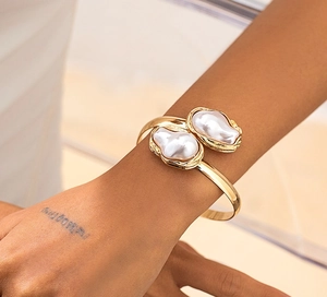 Détail d'un bracelet jonc doré ouvert avec deux perles baroques sur un mannequin