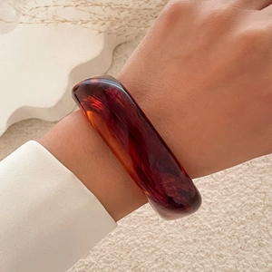 Detailed view of a wide amber resin bracelet with vintage marble texture on a model's wrist
