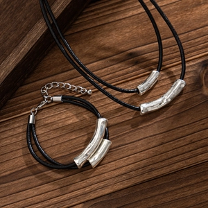 Detail of double-layer black cord necklace with silver curved metal tubes on wood