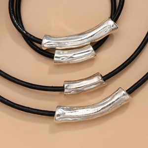 Detail of layered black wax cord necklaces featuring textured silver-tone metal tubes
