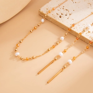 Detail of gold necklace with white pearls, orange faceted beads and metallic bar pendants