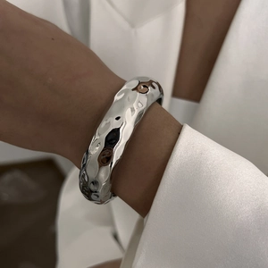 Moderne brede zilveren armband met een unieke gehamerde golfstructuur op metalen oppervlak