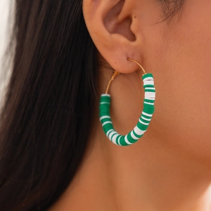 Close-up of bohemian gold hoop earrings with green and white Heishi clay beads