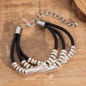 Detail of multi-layer leather bracelet with silver metal beads and curved tubes on wood