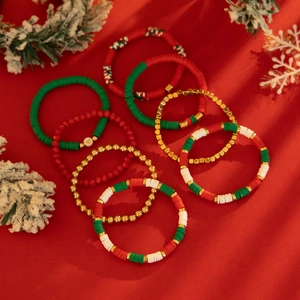 Détail de 9 bracelets de Noël en perles heishi sur fond de velours rouge élégant