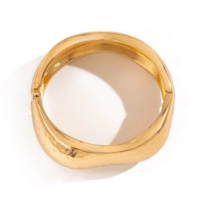 Detailed macro shot of a wide gold metal bracelet with unique irregular hammered texture