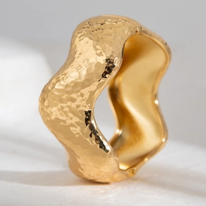 Macro detail of golden hammered texture and irregular wave edges on a wide metal cuff