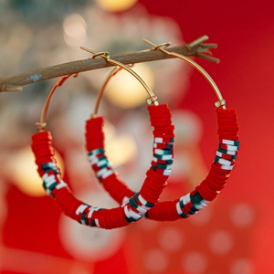 Close-up of Christmas hoop earrings with red, white, and green heishi beads on a golden ring