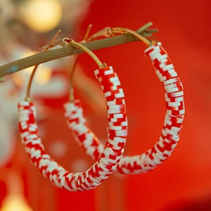 Detail shot of red and white Christmas hoop earrings hanging on a rustic wooden branch