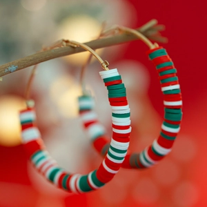 Close-up of Christmas hoop earrings with red, white and green beads on wooden branch