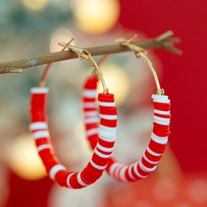 Detail of red and white striped polymer clay hoop earrings on a wooden branch