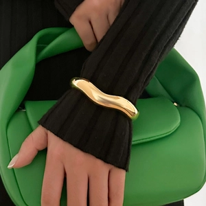 Detail of chunky gold wavy bangle featuring a polished metallic finish on a model wrist