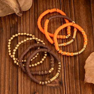 Detail von böhmischen Stapelarmbändern mit orangefarbenen Tonperlen und goldenen Metallakzenten