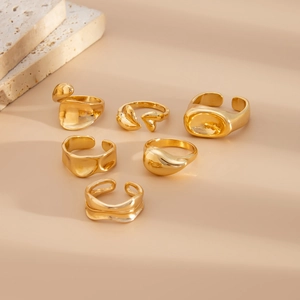 Set of six gold organic irregular rings with lava texture on warm beige background