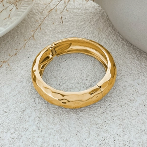 Detailopname van gouden brede armband met gehamerd ontwerp en handige veerscharnier