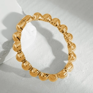 Detail of 18K gold-plated bubble texture bracelet with hinge on a textured stone background