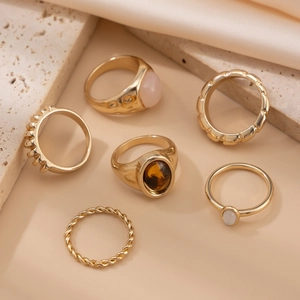 Detailansicht eines sechsteiligen goldenen Ring-Sets mit Edelsteinen auf Seide und Stein