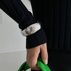 Detail of wide silver hammered metal bracelet worn over black textured knit sleeve