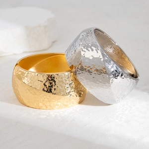 Detail of wide metal bracelets with hammered texture in gold and silver finish