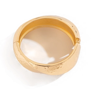 Close-up of golden wide cuff bracelet featuring hammered texture and side hinge detail