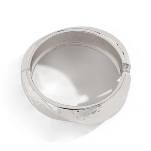 Detail of wide silver metal bracelet with textured hammered finish and hinge closure